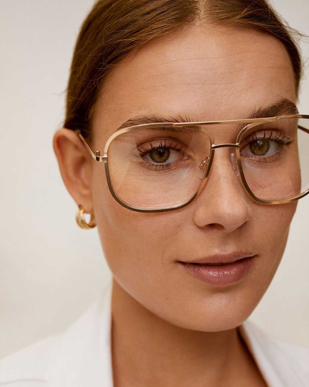 Close view of woman wearing oversized gold Aviator eyeglasses and white blouse
