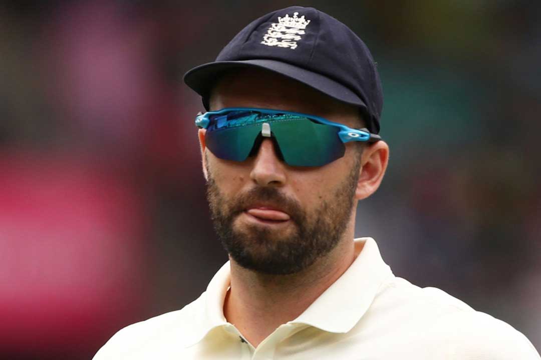 English cricketer Mark Wood wearing blue cap white uniform and blue tinted sports sunglasses frame