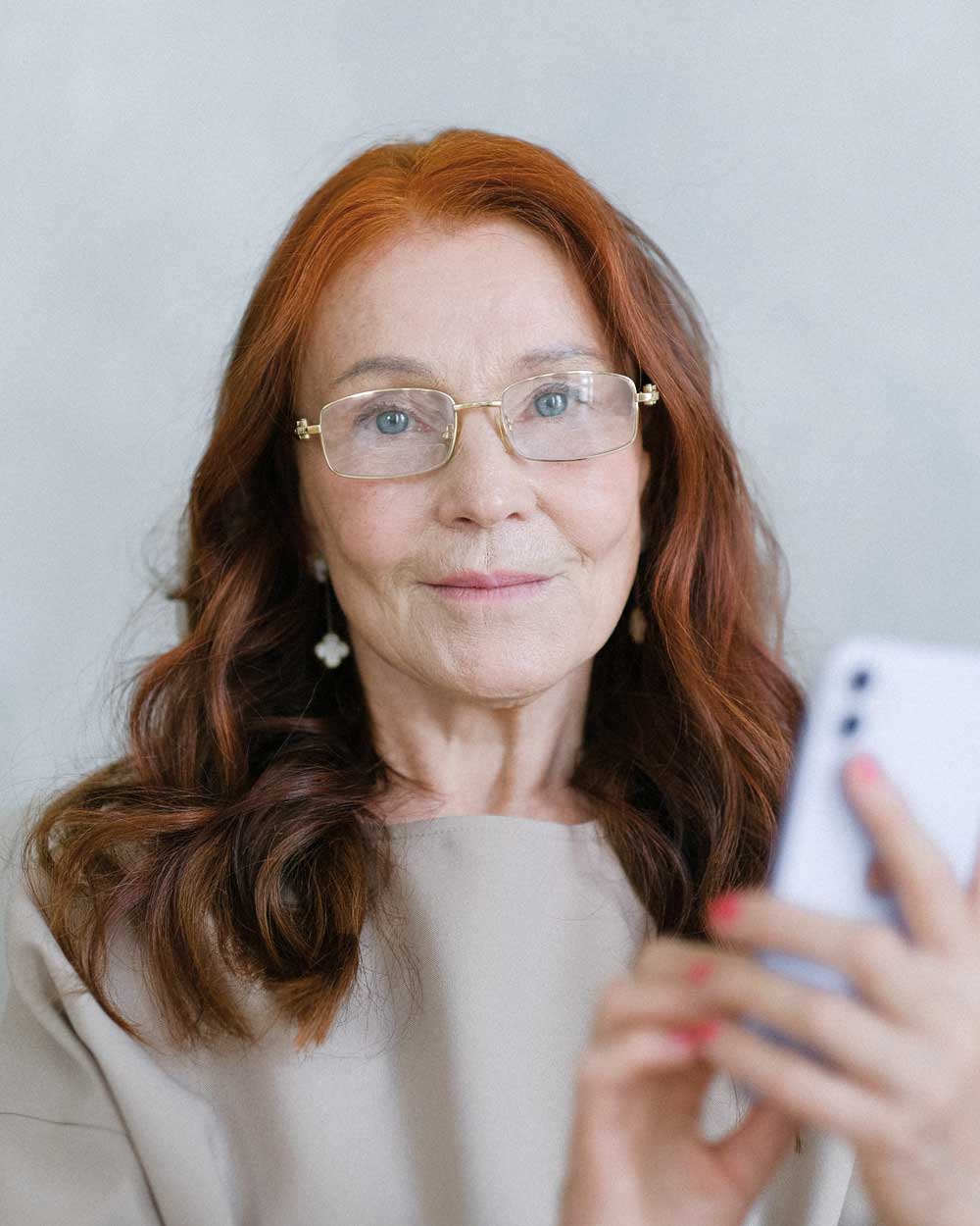 Ginger haired women wearing rimless spectacles holding her cell phone