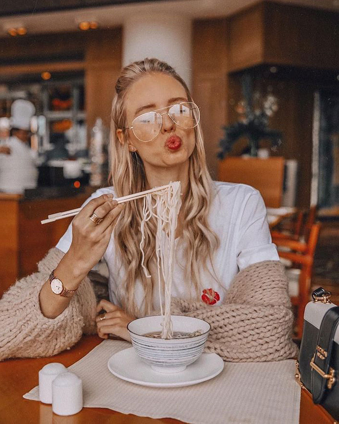 Golden blonde female pouting her lips whilst eating noodles in a restaurant wearing Aviator wire glasses frame