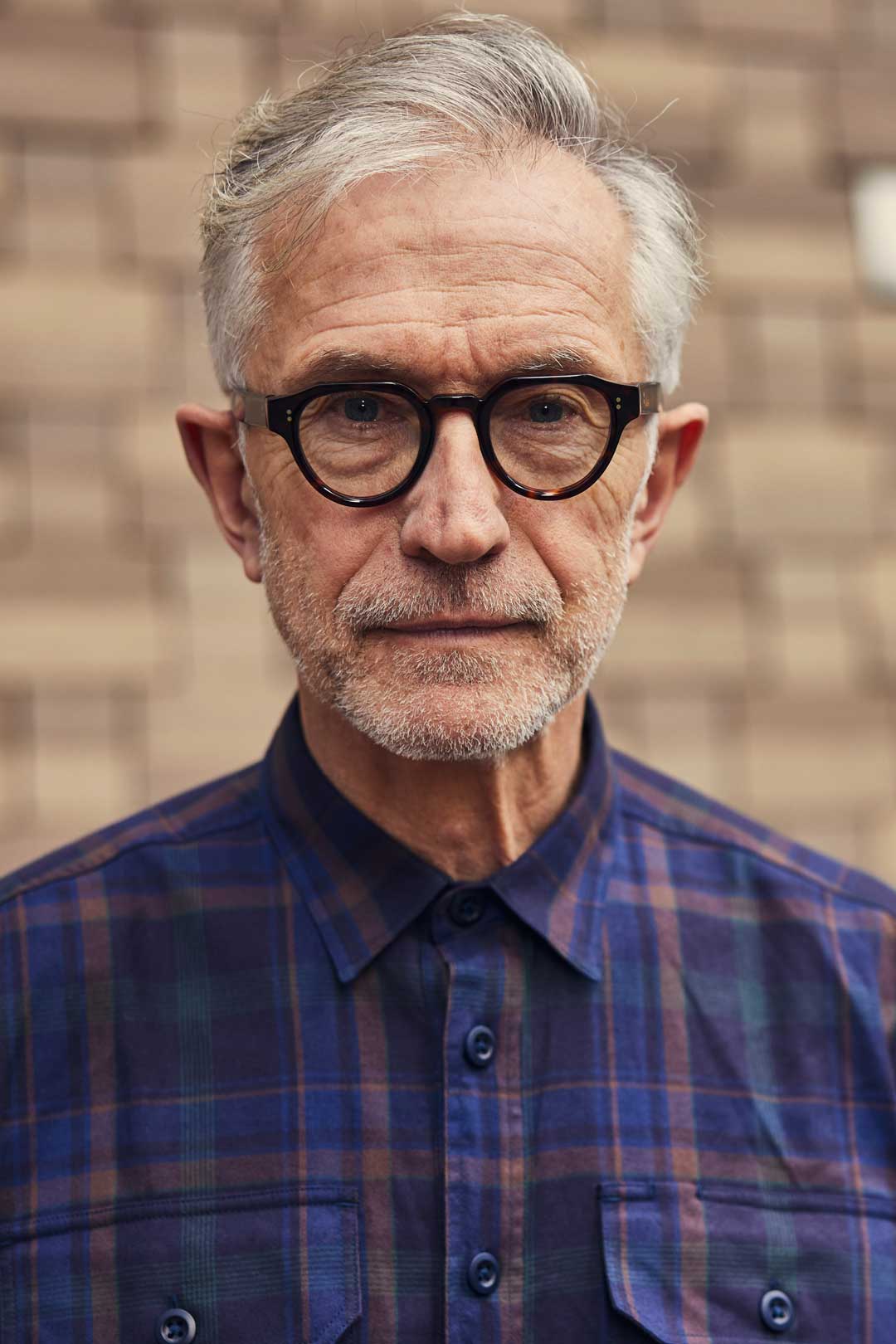 Grey haired man wearing blue shirt and thick eyeglasses frame outside in street