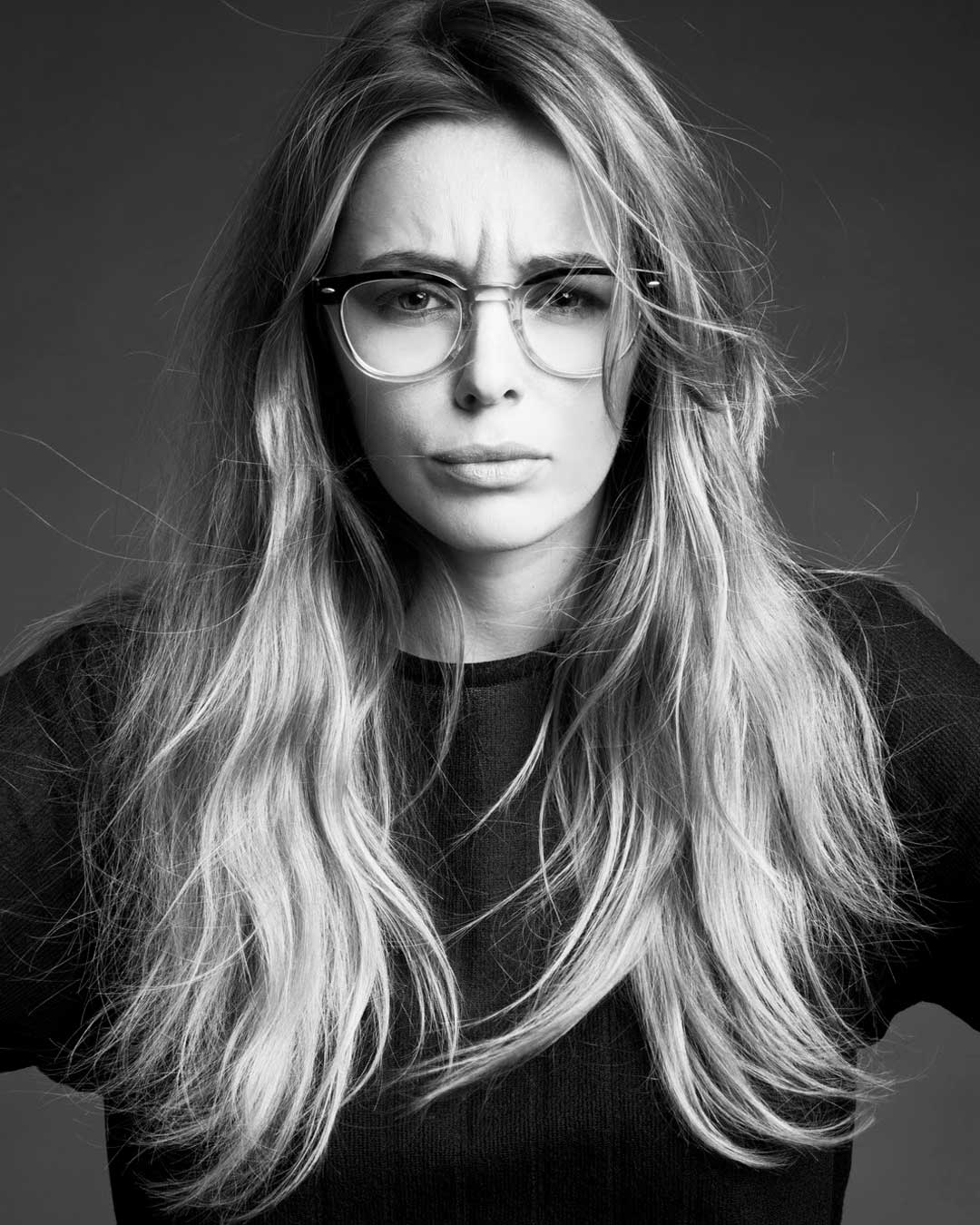 Greyscale image of woman with long light hair looking confused wearing gradient acetate glasses frame