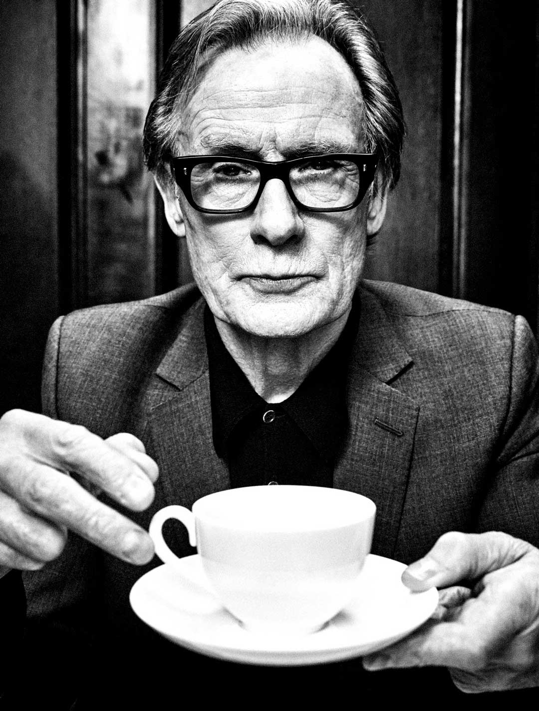 Greyscale portrait of mature gentleman holding tea cup wearing thick black spectacles