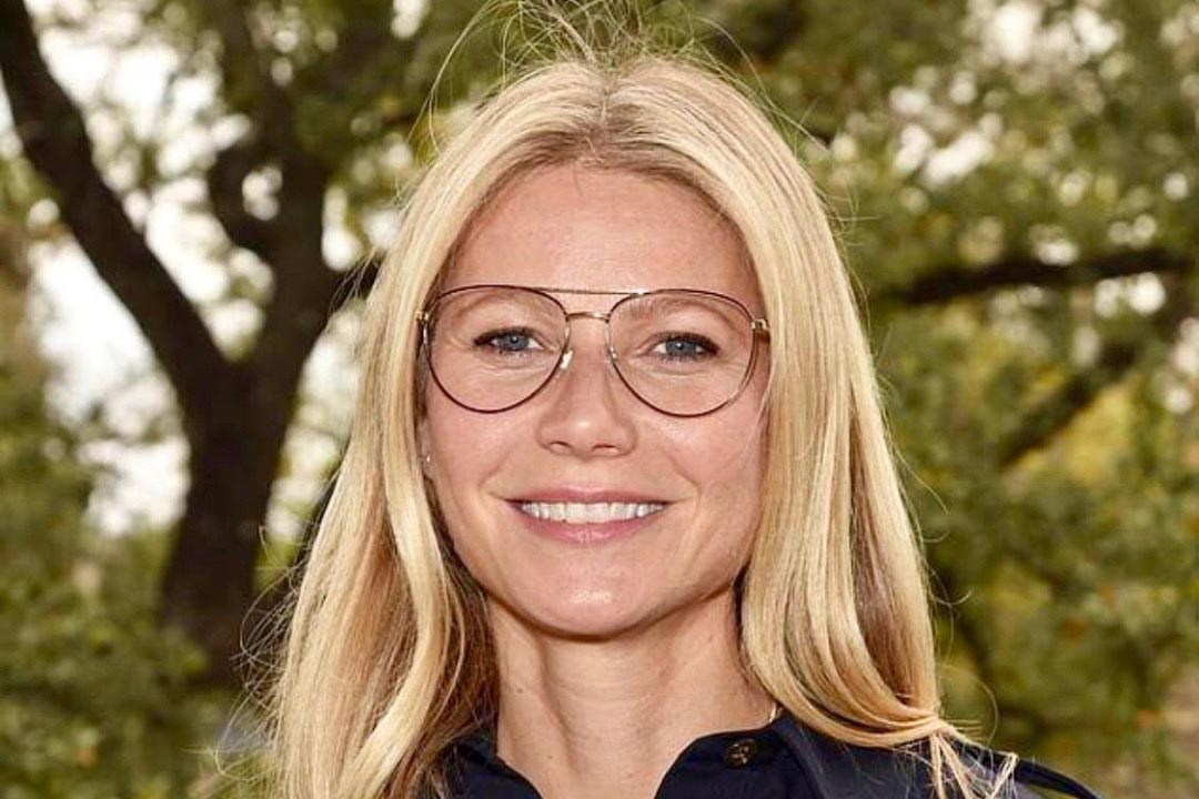 Gwyneth Paltrow wearing double bridge wire glasses smiling outside in front of trees