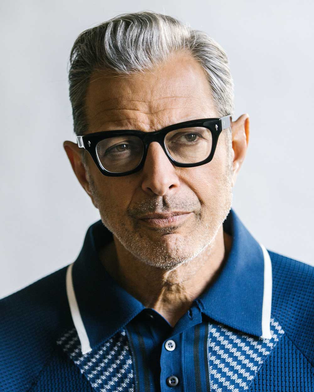 Jeff Goldblum wearing chunky rectangular eyeglasses frame and blue polo shirt