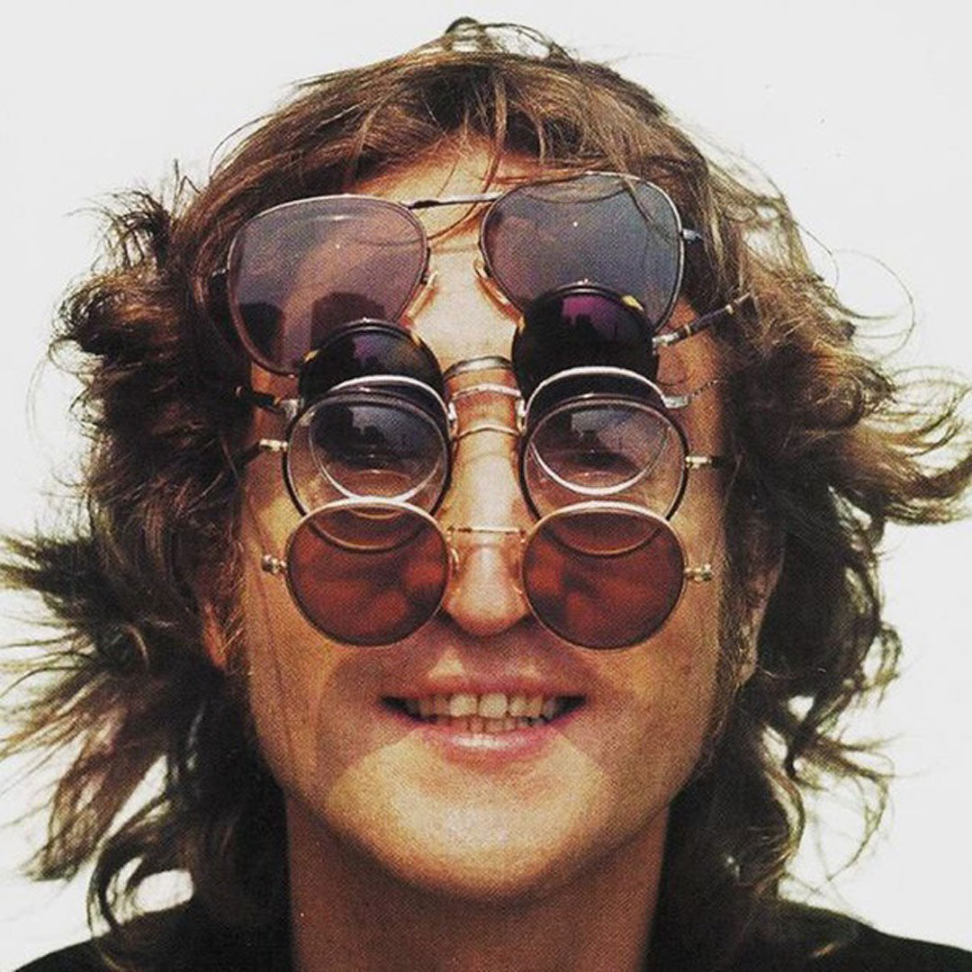 John Lennon wearing numerous round rim spectacles and sunglasses all on his head and face at once