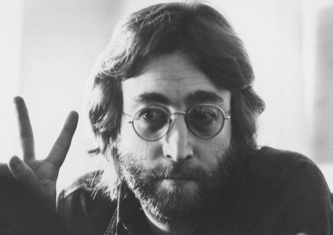 John Lennon with long hair and beard making peace symbol with his fingers
