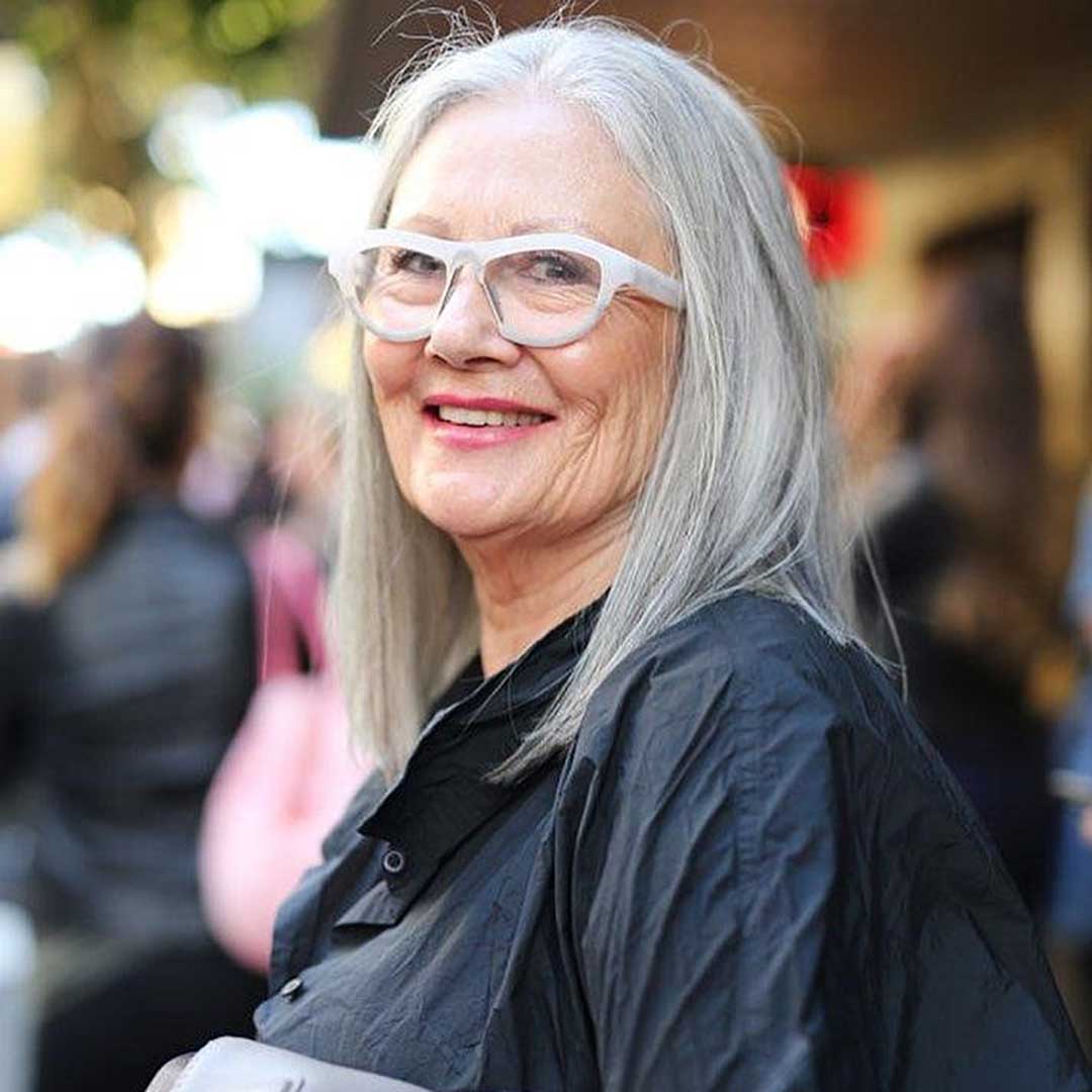 Lady in street with long grey haircut wearing blue jacket and white eyeglasses frame