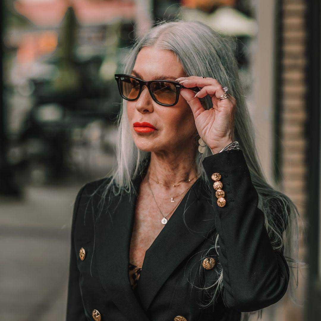 Lady in street with very long grey hair touching her black Ray Ban sunglasses