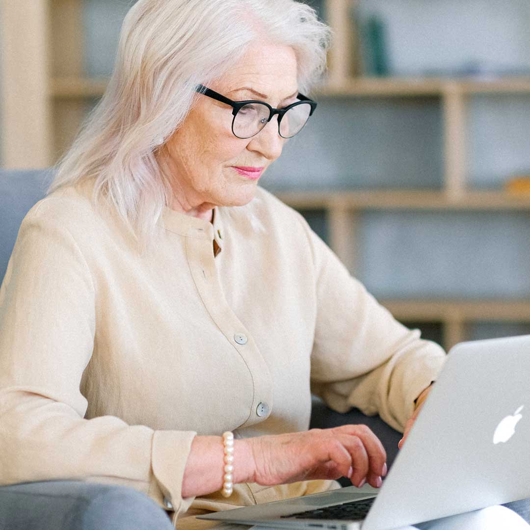 Lady with long white hair and brow line eyeglasses using her laptop computer