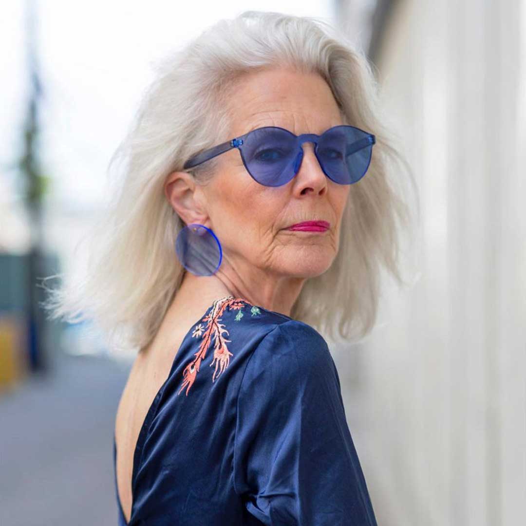 Lady with long white hair looking over her shoulder wearing blue blouse and blue plastic glasses fashion frame