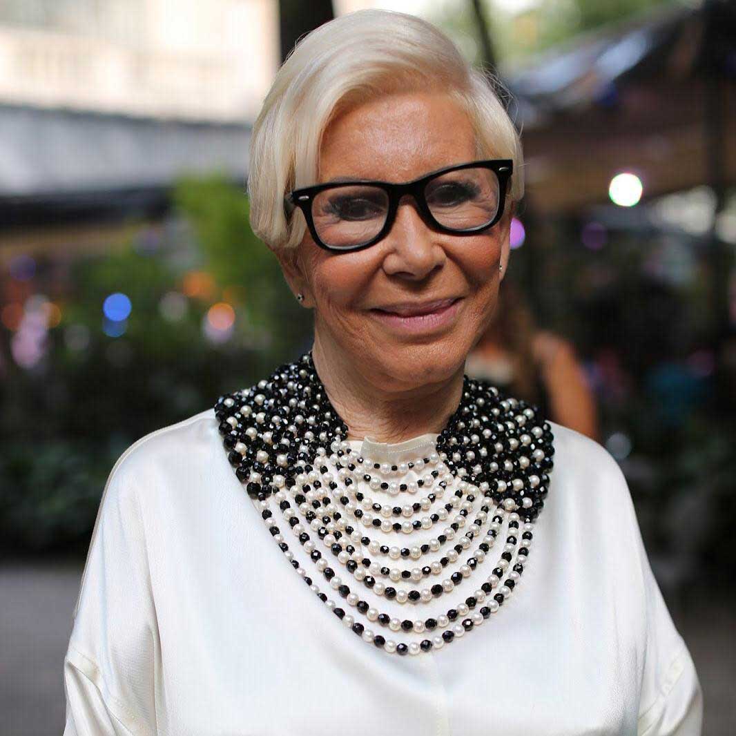 Lady with sideswept Pixie haircut wearing white top necklace and thick black spectacle frame