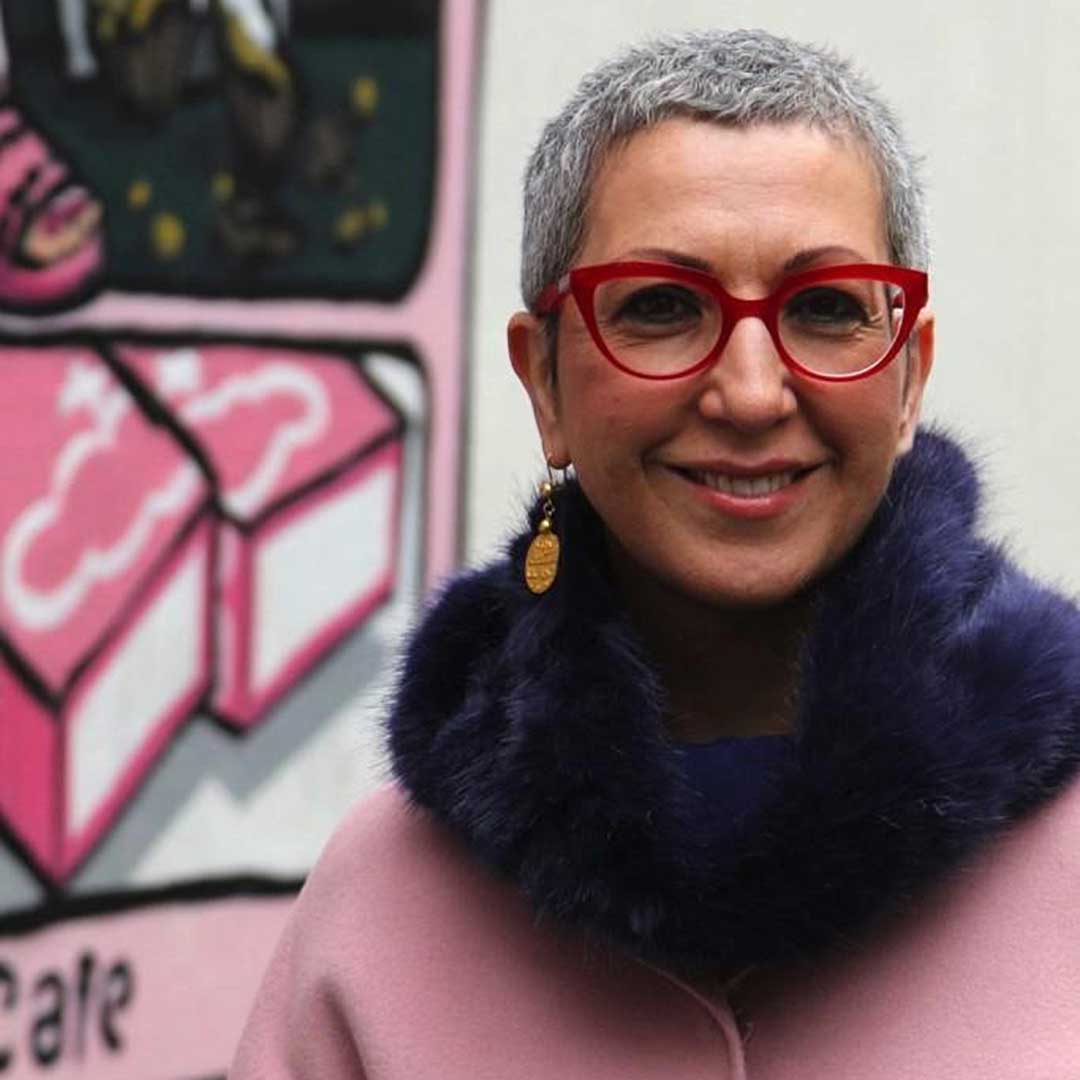 Lady with very short grey hair smiling wearing fur coat and red cat eye spectacle frame