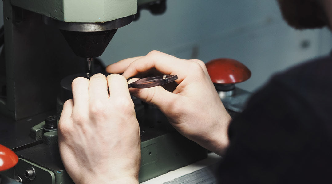 Male worker attaching hinges to a grey spectacle frame using a green rivetting machine