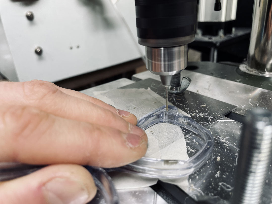 Male worker drilling holes through a crystal clear sunglasses frame