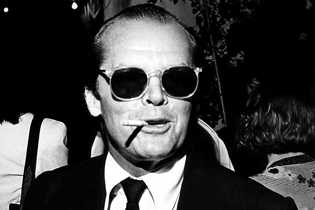 Man at a dinner party smoking a cigarette wearing round frame sunglasses