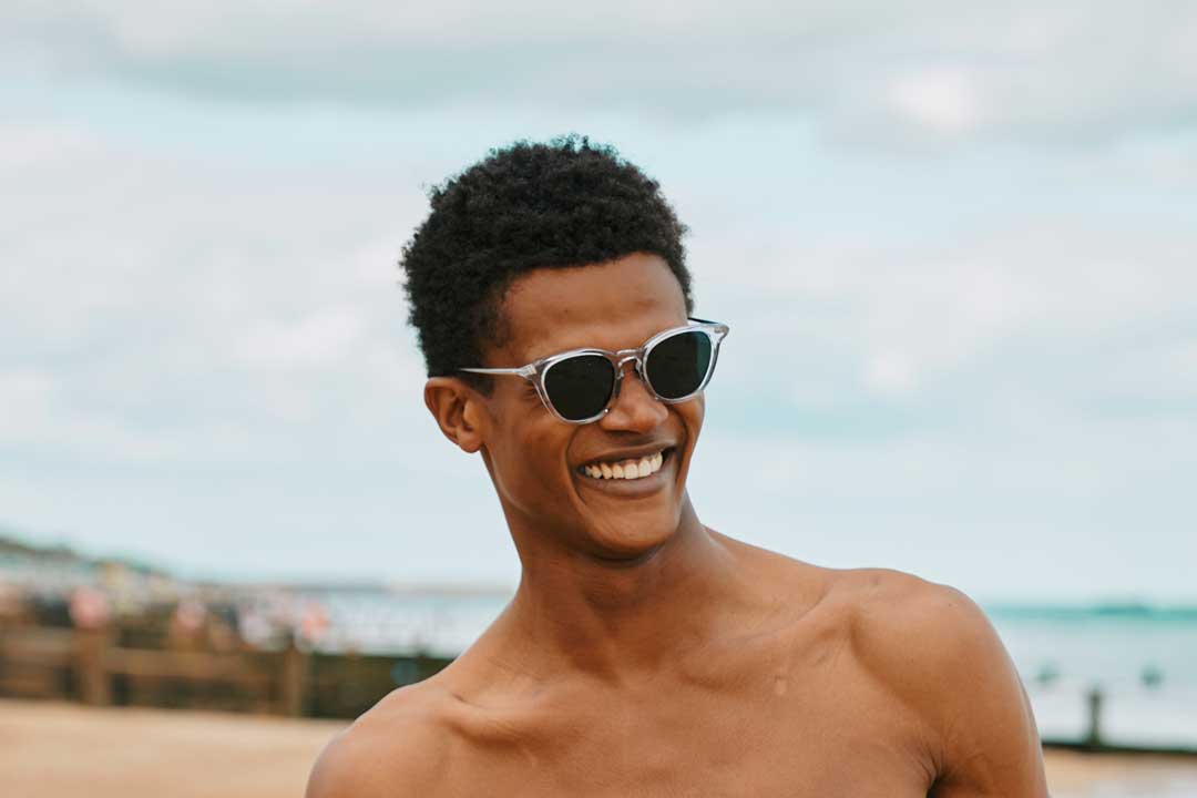 Man at beach smiling wearing crystal frame sunglasses on sunny day