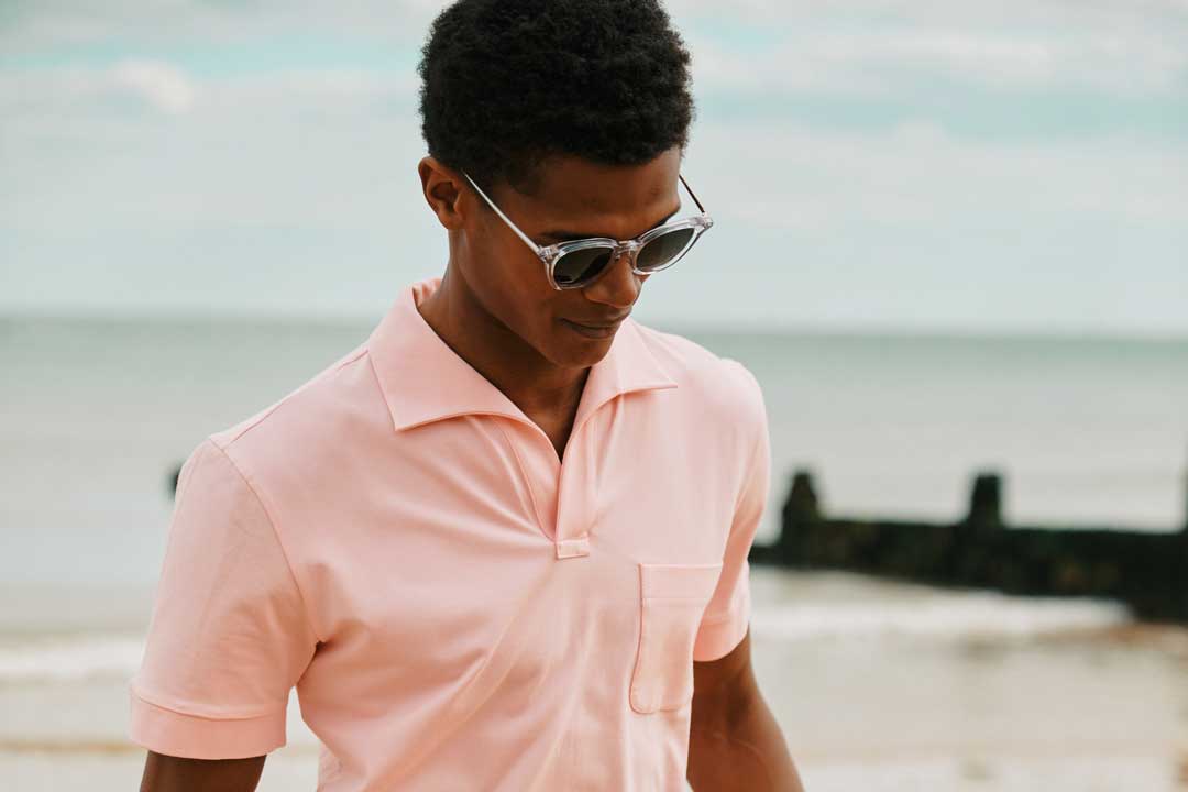 Man at beach wearing pink shirt and sunglasses looking downwards
