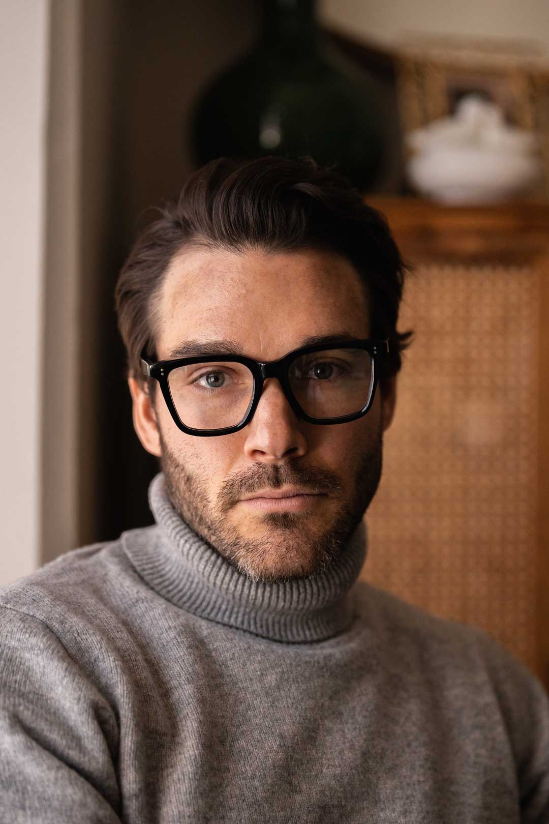 Man in grey sweater wearing thick frame square eyeglasses