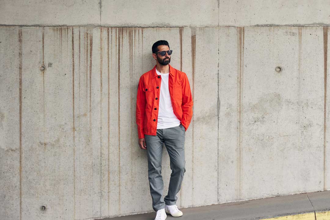 Man in orange jacket and sunglasses leaning against concrete wall