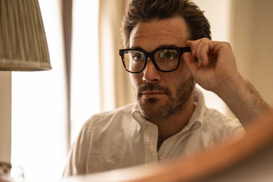 Man looking in mirror adjusting his thick eyeglasses frame