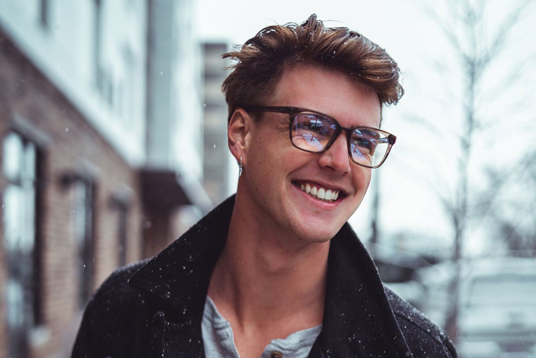 Man smiling walking down a snowy street wearing winter coat and glasses frame