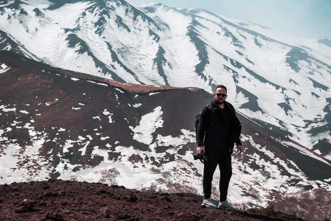 Man standing in snow covered mountains wearing jacket and sunglasses on bright sunny day