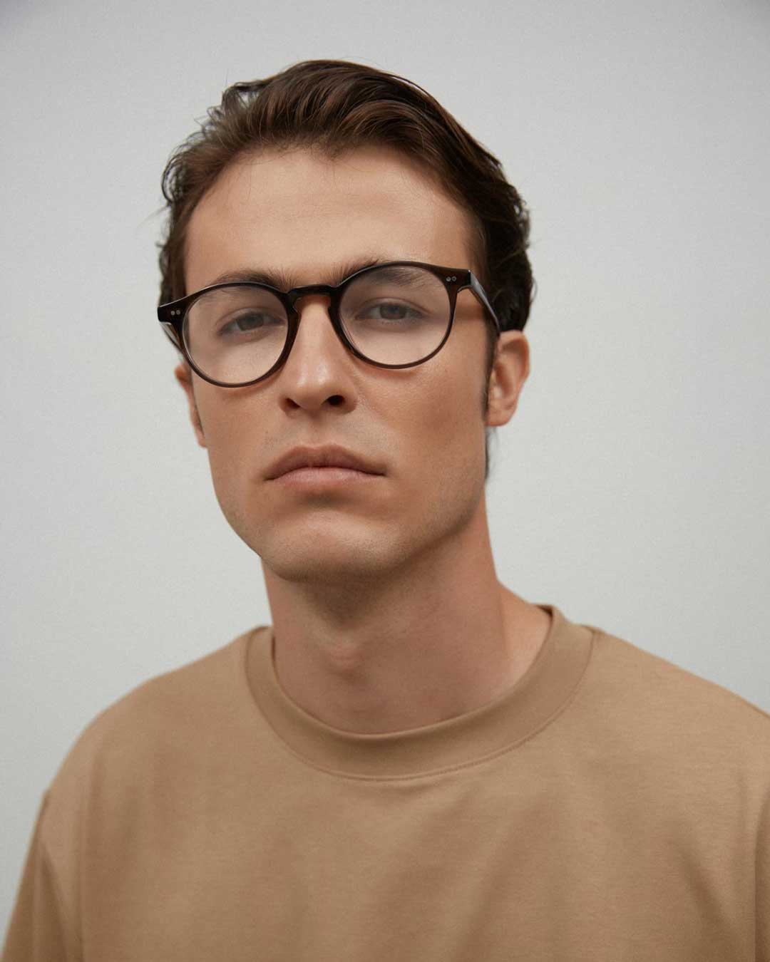 Man wearing beige coloured Tshirt with round brown tortoise eyeglasses frame