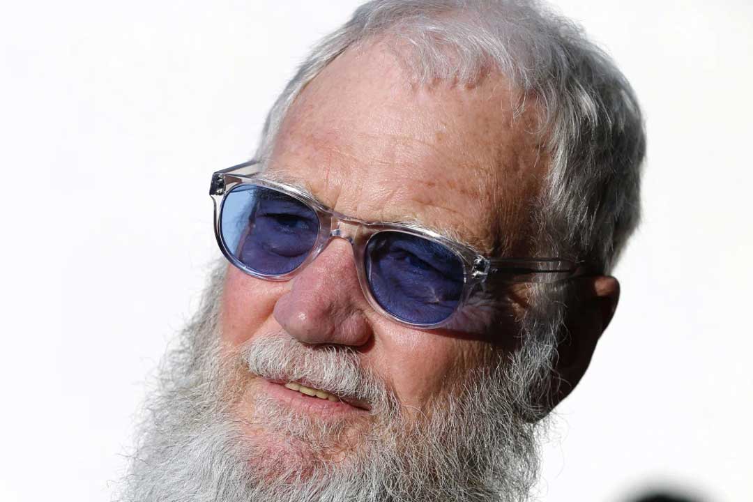 Man with grey hair and beard wearing clear sunglasses with purple tinted lenses