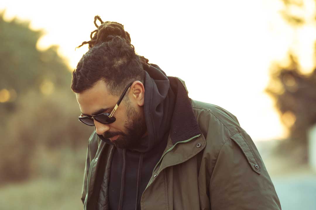 Man with long hair and sunglasses wearing thick green coat on cold day