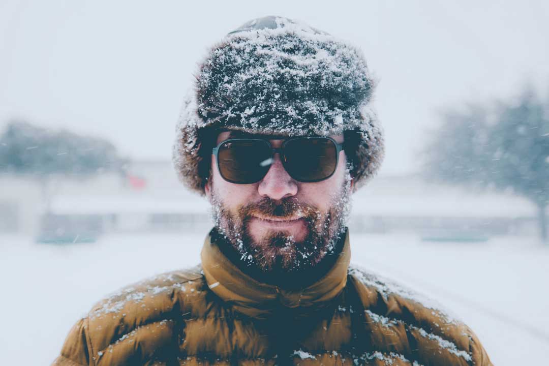 Man with wooly hat beard and sunglasses frame standing outside on snowy day