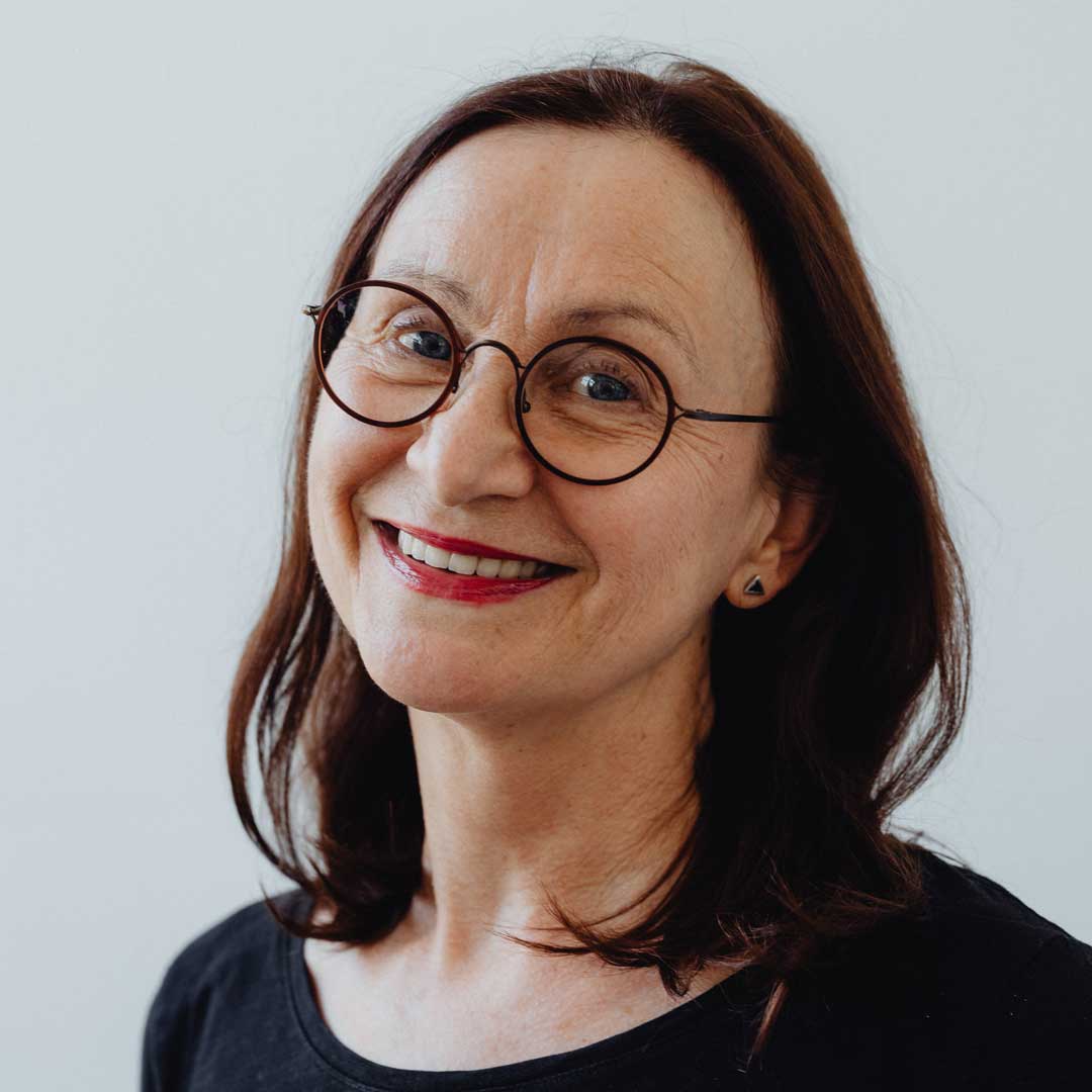 Mature lady with auburn hair smiling wearing black circle glasses frame