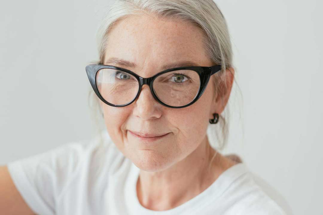 Mature lady with grey hair wearing black cat eye glasses frame smiling