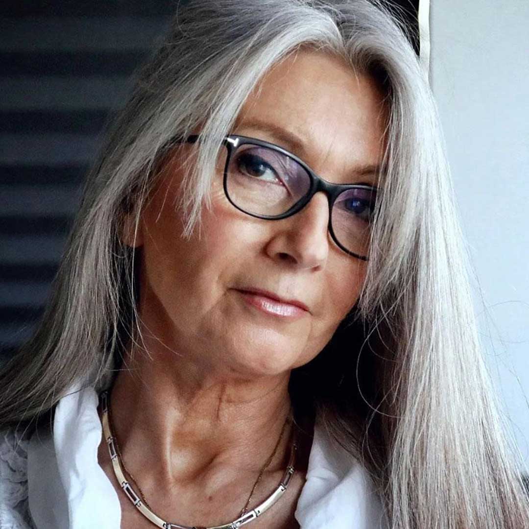 Mature lady with long grey hair with bangs wearing rectangular black glasses