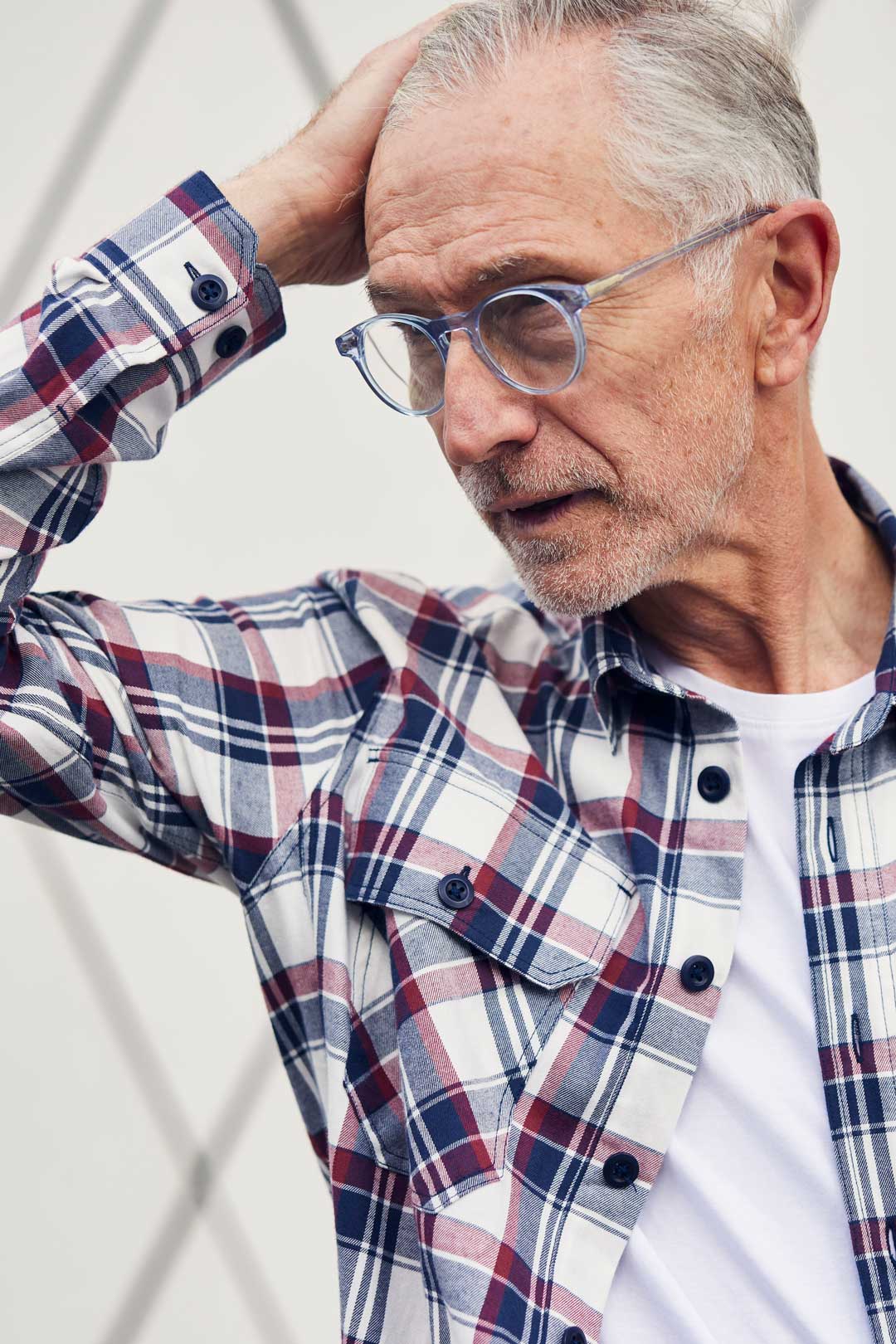 Mature man wearing round blue crystal eyeglasses frame running his hand through his grey hair