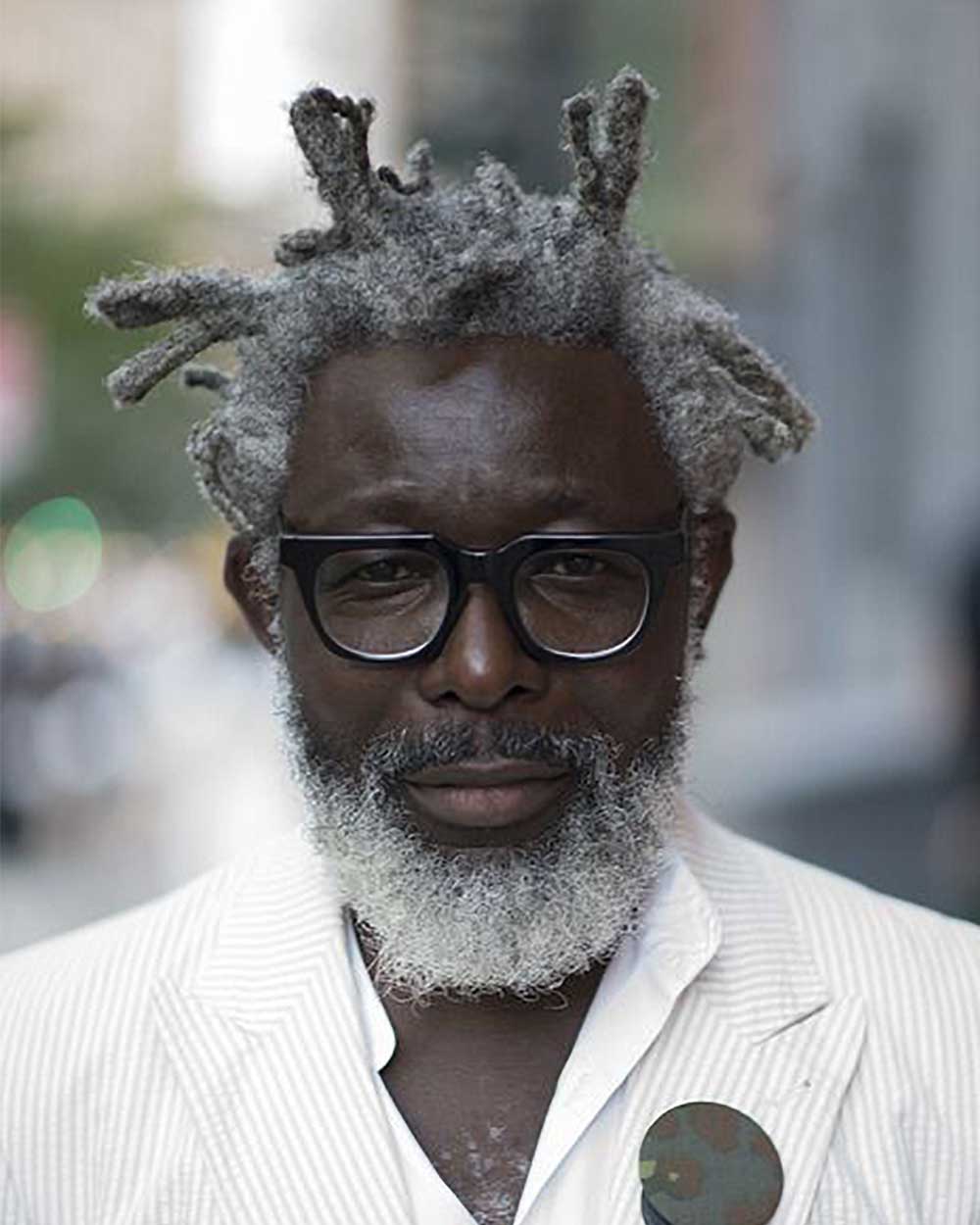 Mature man with grey afro hair wearing thick black eyeglasses frame