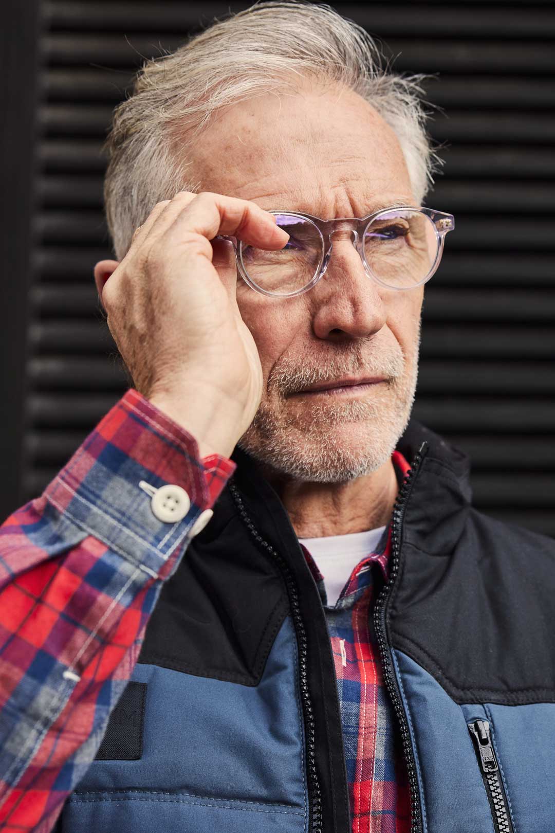 Mature man with grey hair adjusting his round clear eyeglasses frame with one hand