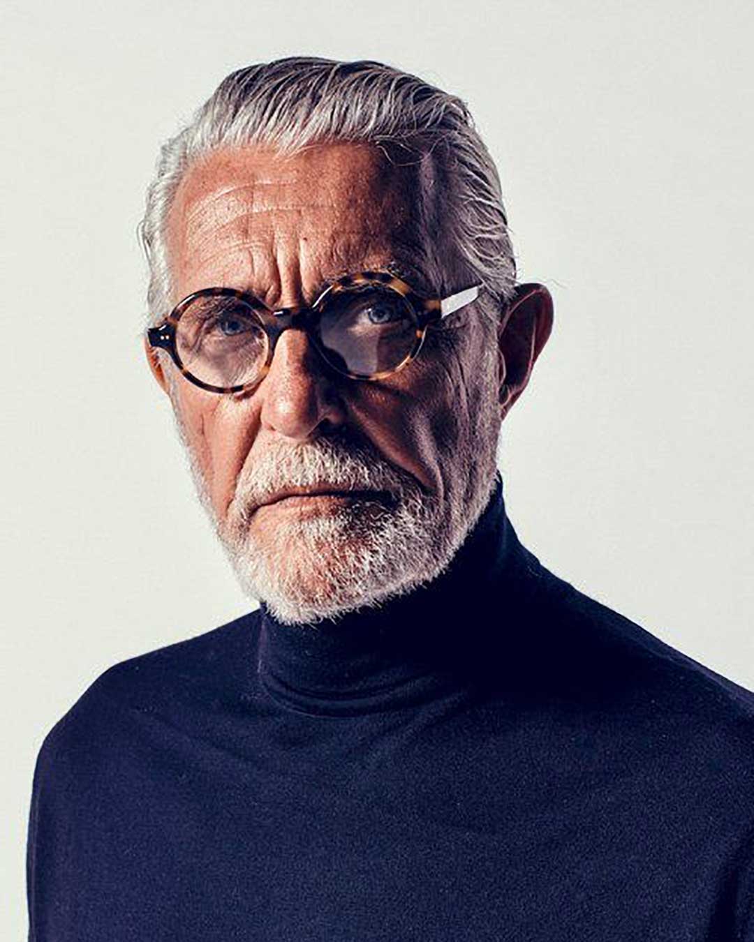 Mature man with grey hair wearing blue sweater and round tortoise spectacles