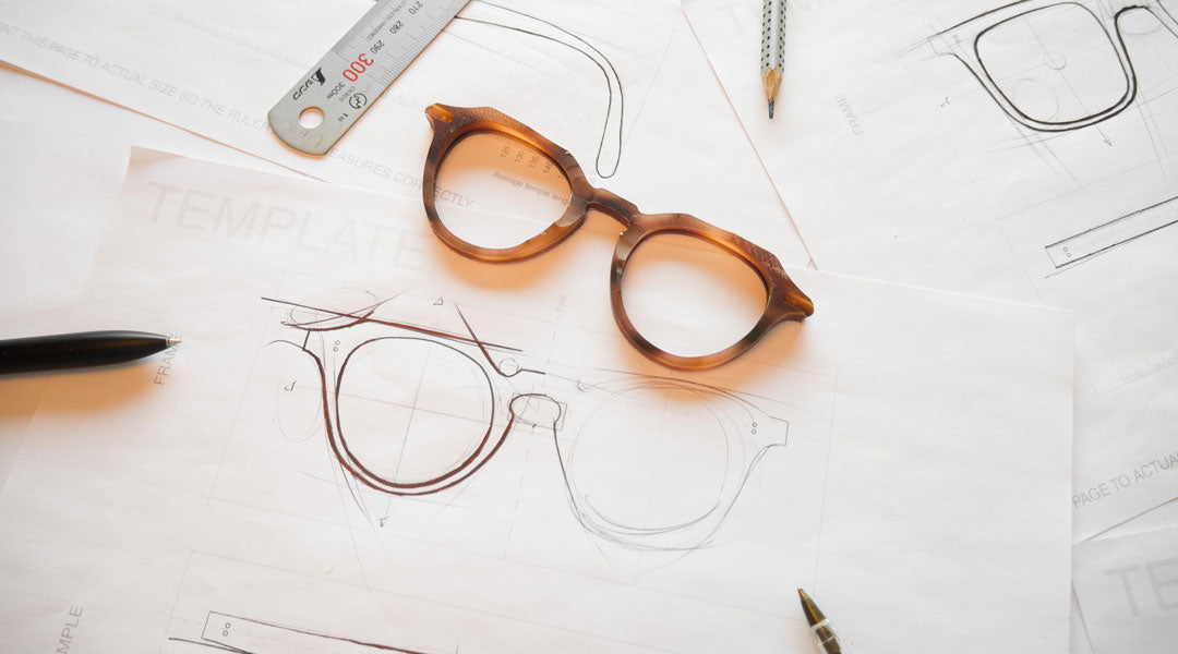 Octagonal orange sunglasses frame surrounded by drawing utensils lying upon white paper templates