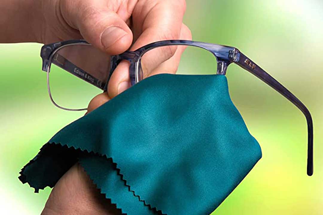 Person cleaning a pair of eyeglasses with teal coloured microfibre cloth