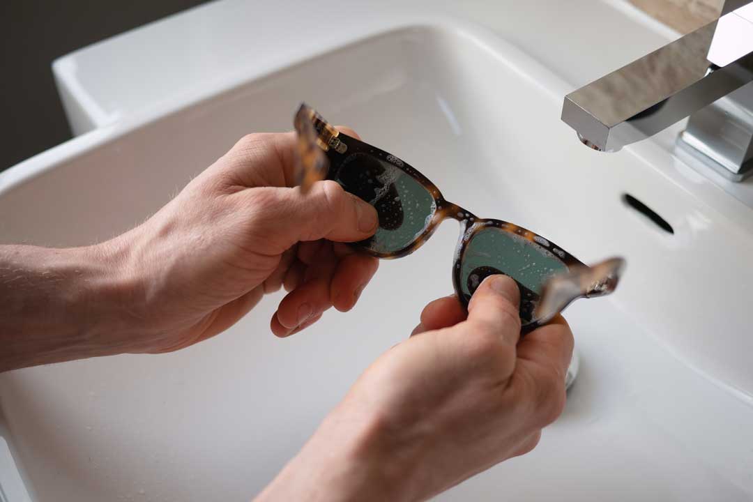 Person cleaning tortoise sunglasses frame in white wash basin