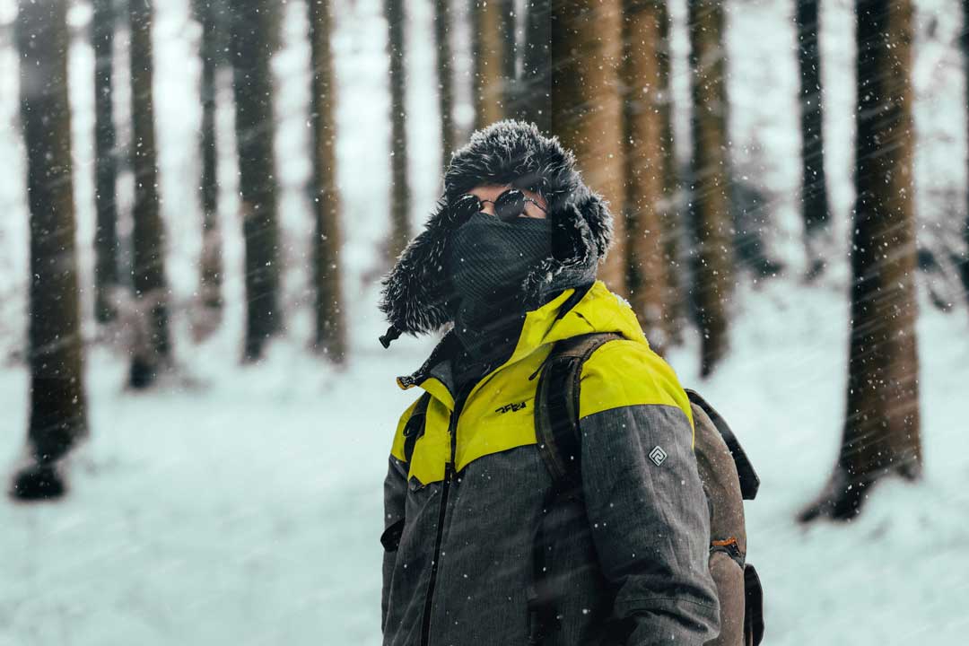 Person standing in blizzard wearing yellow jacket fury hat and round sunglasses