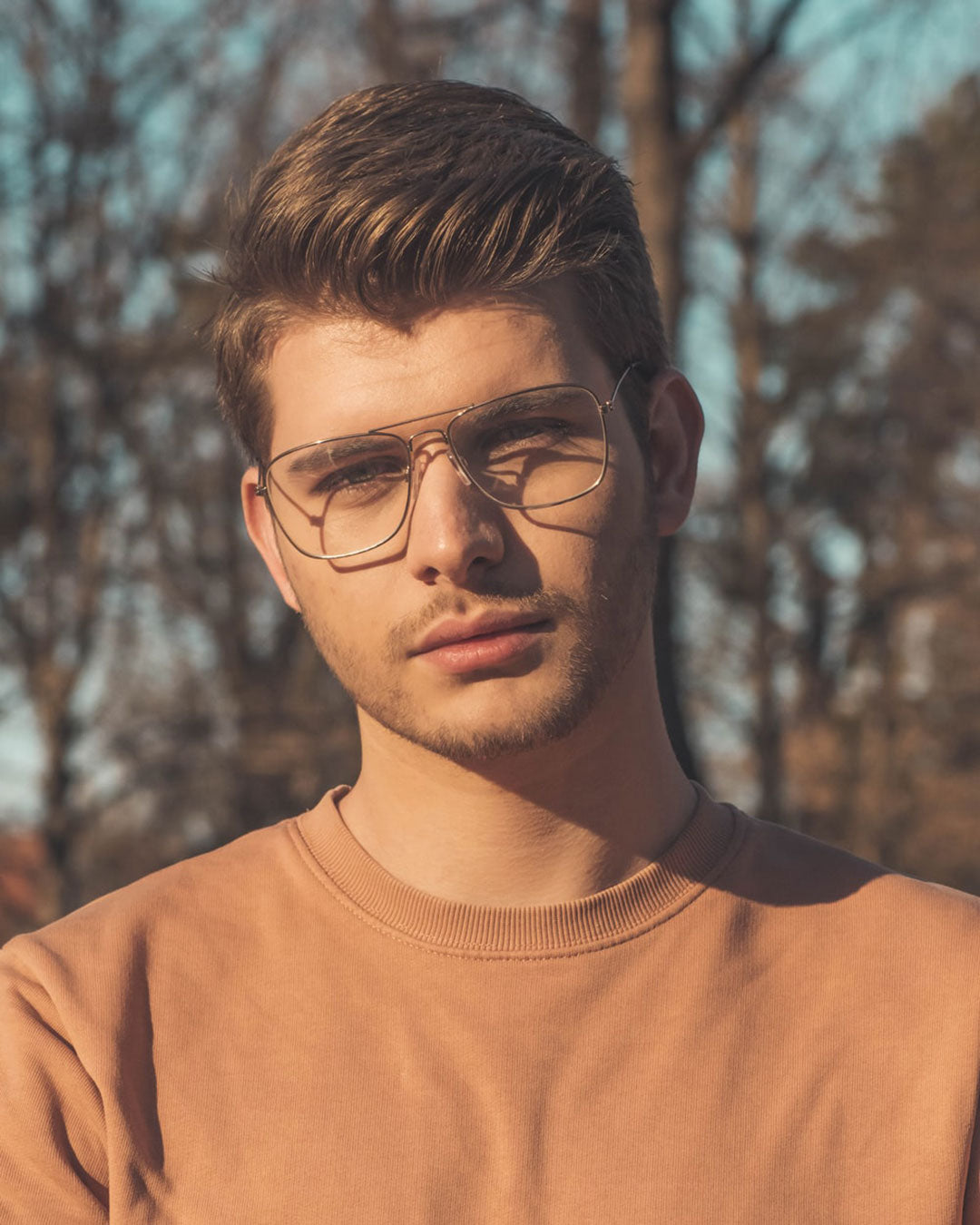 Portrait of blonde male wearing wire Aviator spectacles and orange jumper