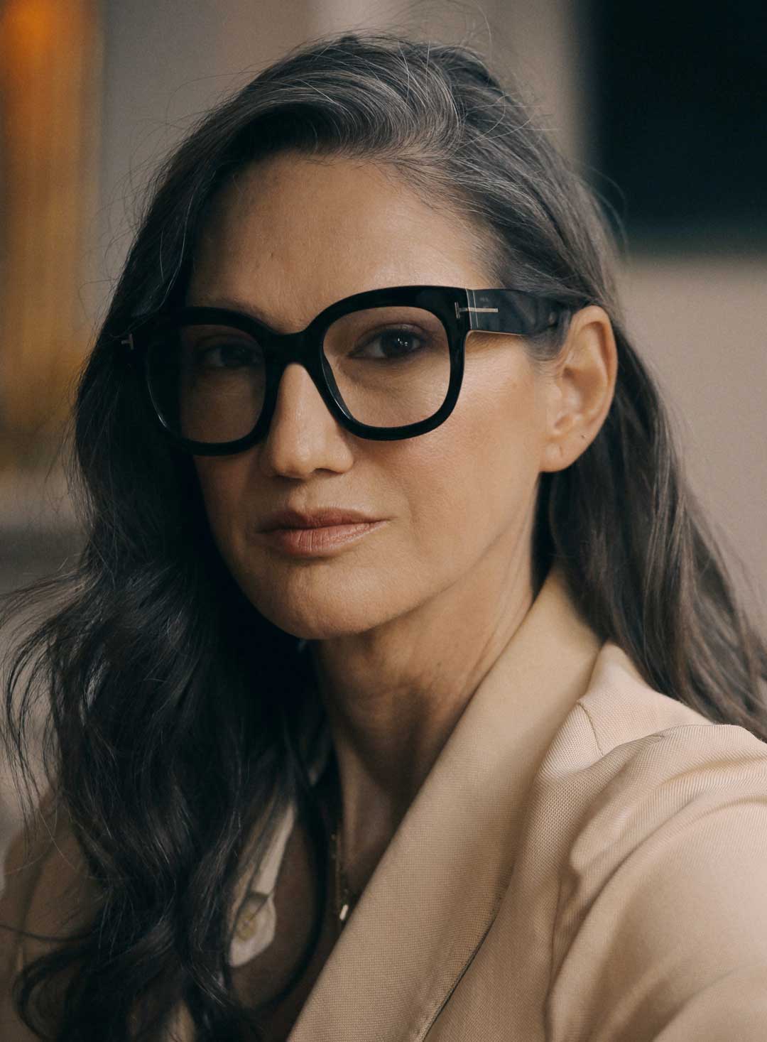 Portrait of mature woman with dark hair wearing beige coat and thick black cat eye glasses frame