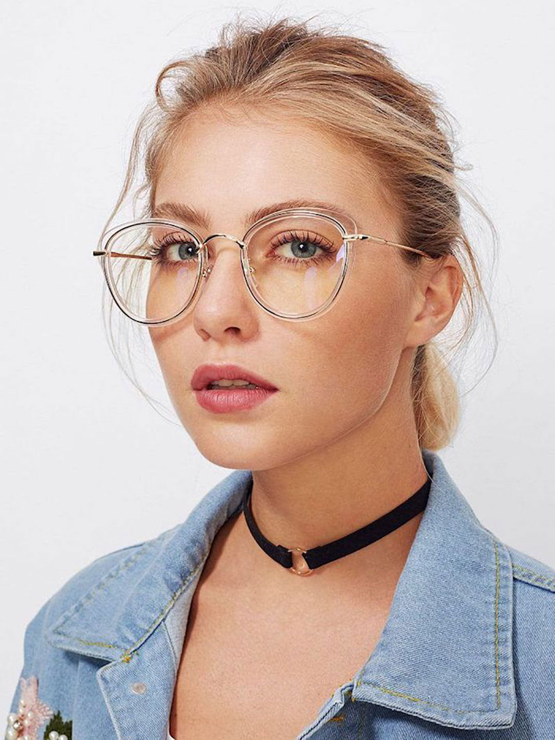 Portrait of pretty blonde lady with tied back blonde hair wearing large clear glasses frame and denim shirt looking at viewer