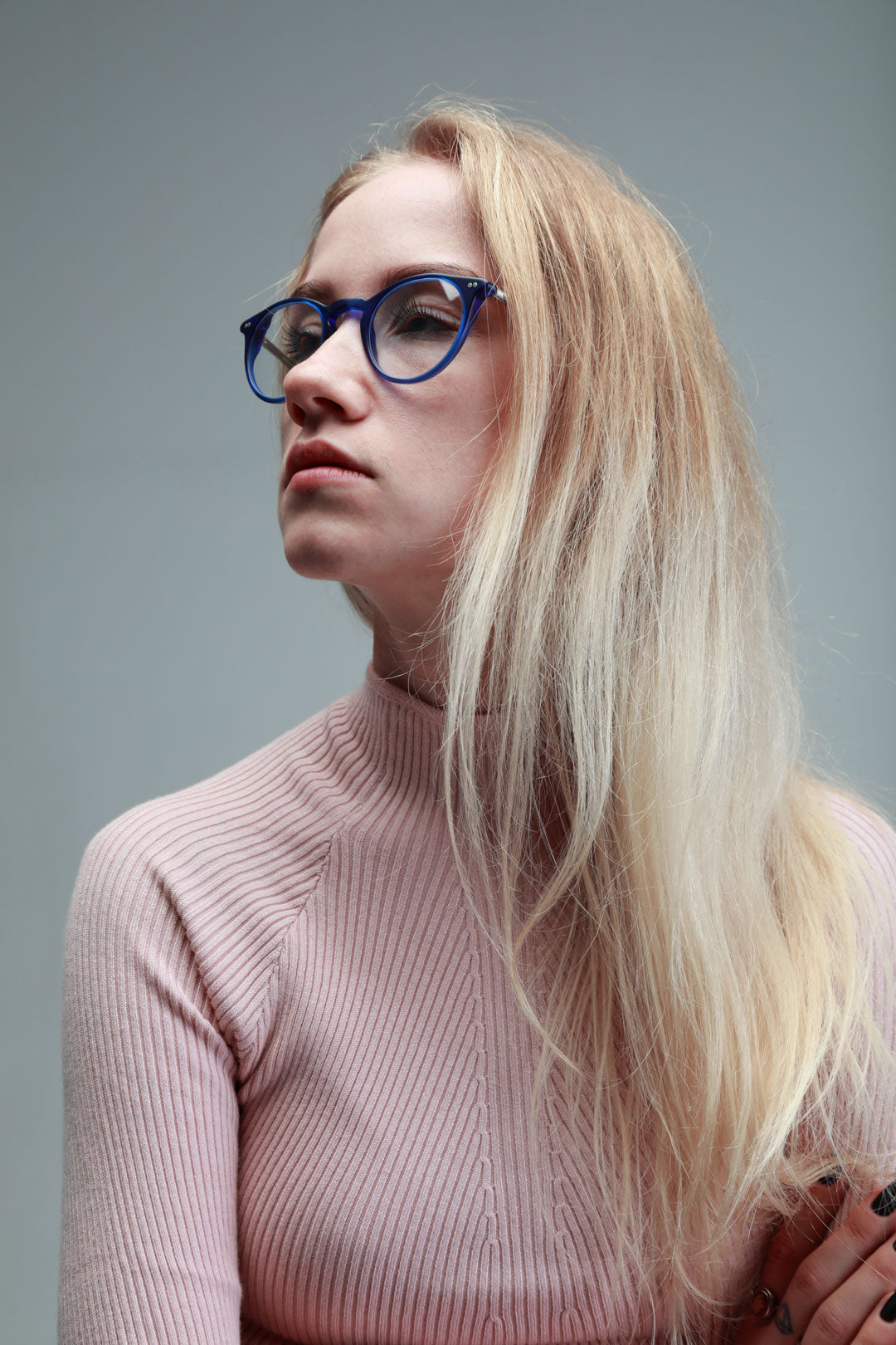 Portrait of young blonde female in pink top and round blue spectacle frame looking sideways