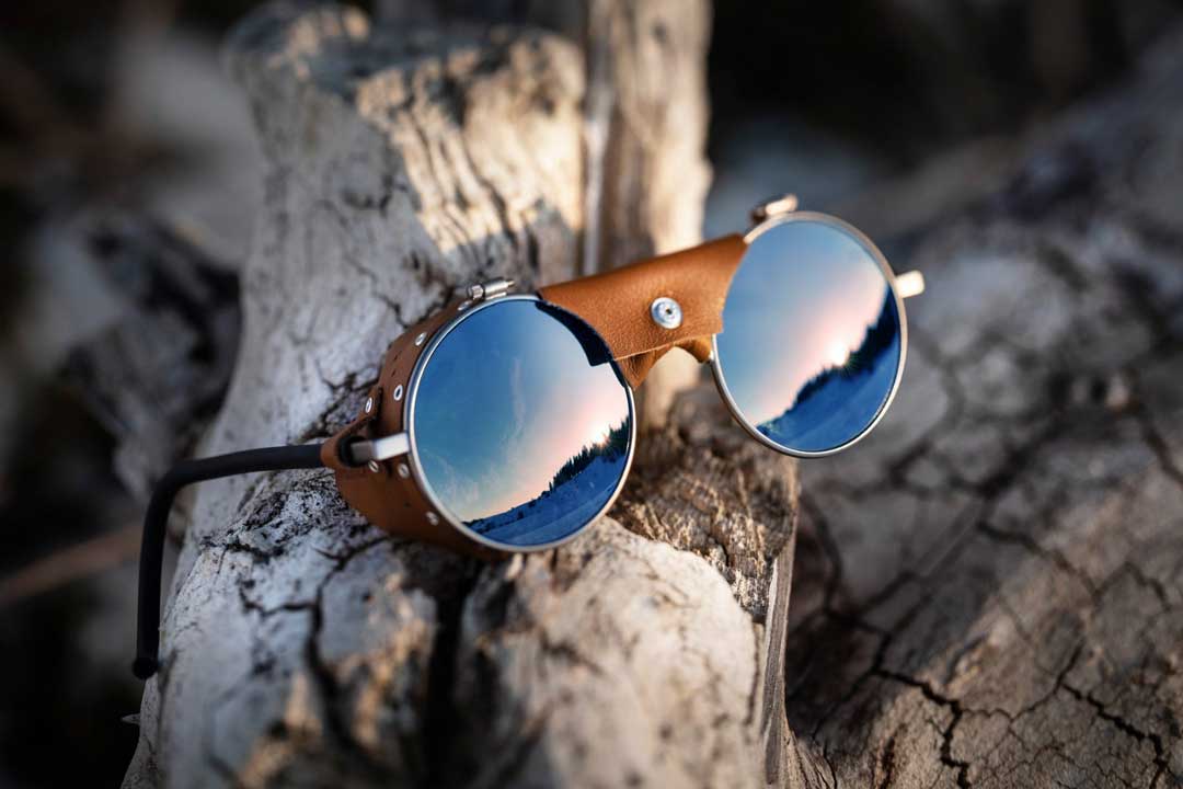Round metal sunglasses with blue mirrored lenses lying on tree branch outside on sunny day