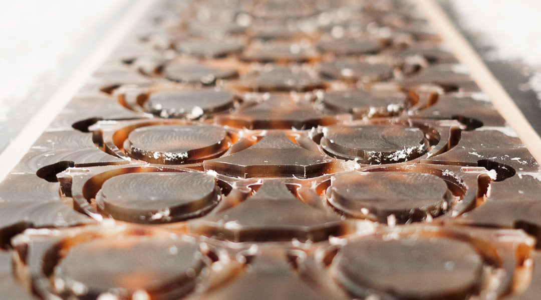 Rows of tortoise acetate glasses frames being manufactured from a large plastic sheet inside an industrial machine enclosure