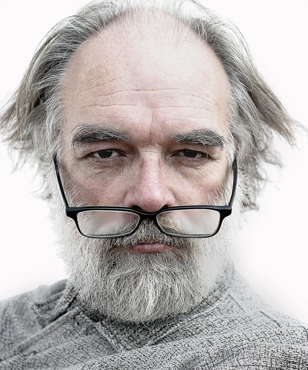 Serious looking man with long grey hair with his glasses humorously hanging off the end of his nose