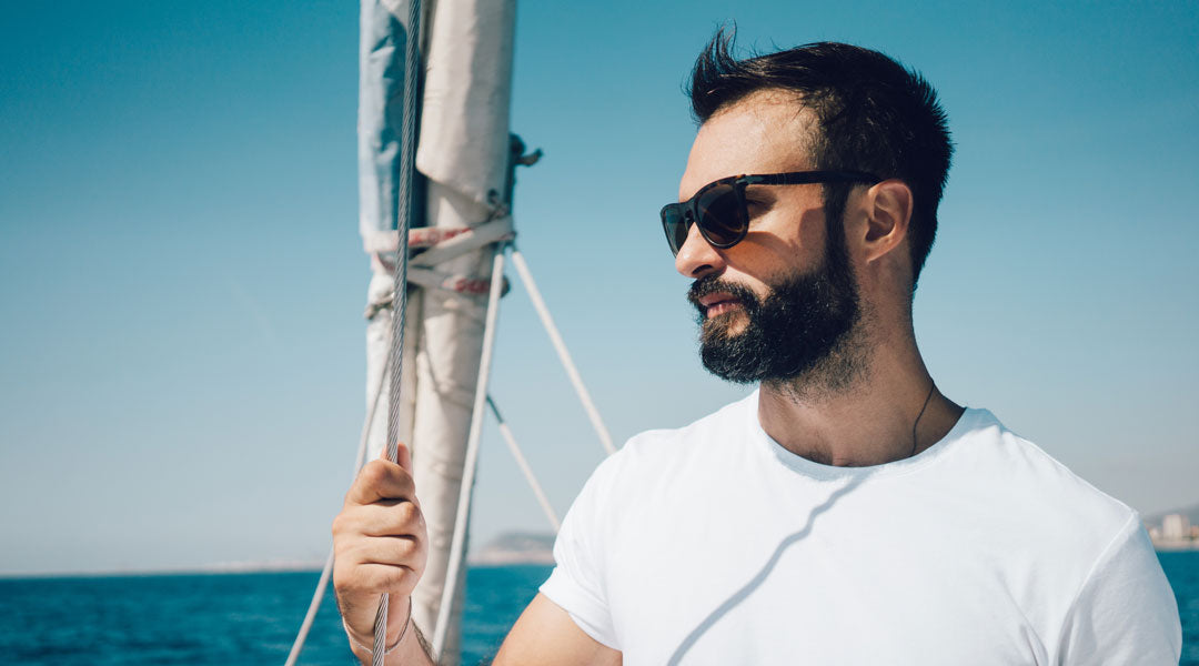Side view of bearded man on sail yacht wearing polarised sunglasses and white shirt